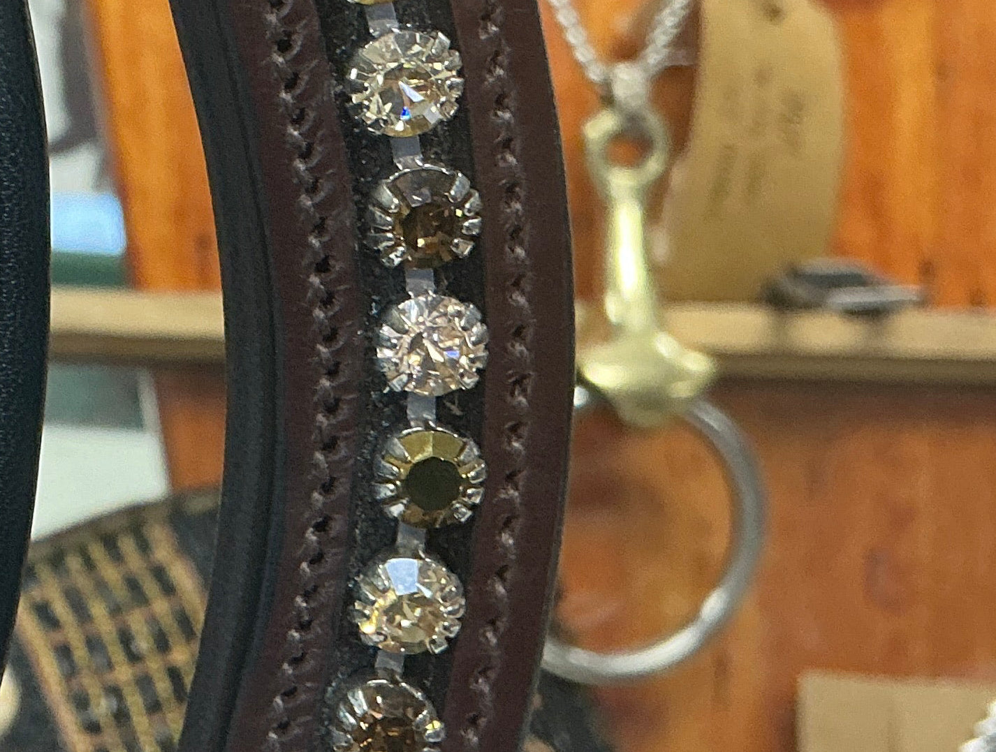Close-up of Peaches and cream brown band vertically, decorated with rows of rhinestones. The visible straps are black and dark brown, with clear and iridescent stones.
