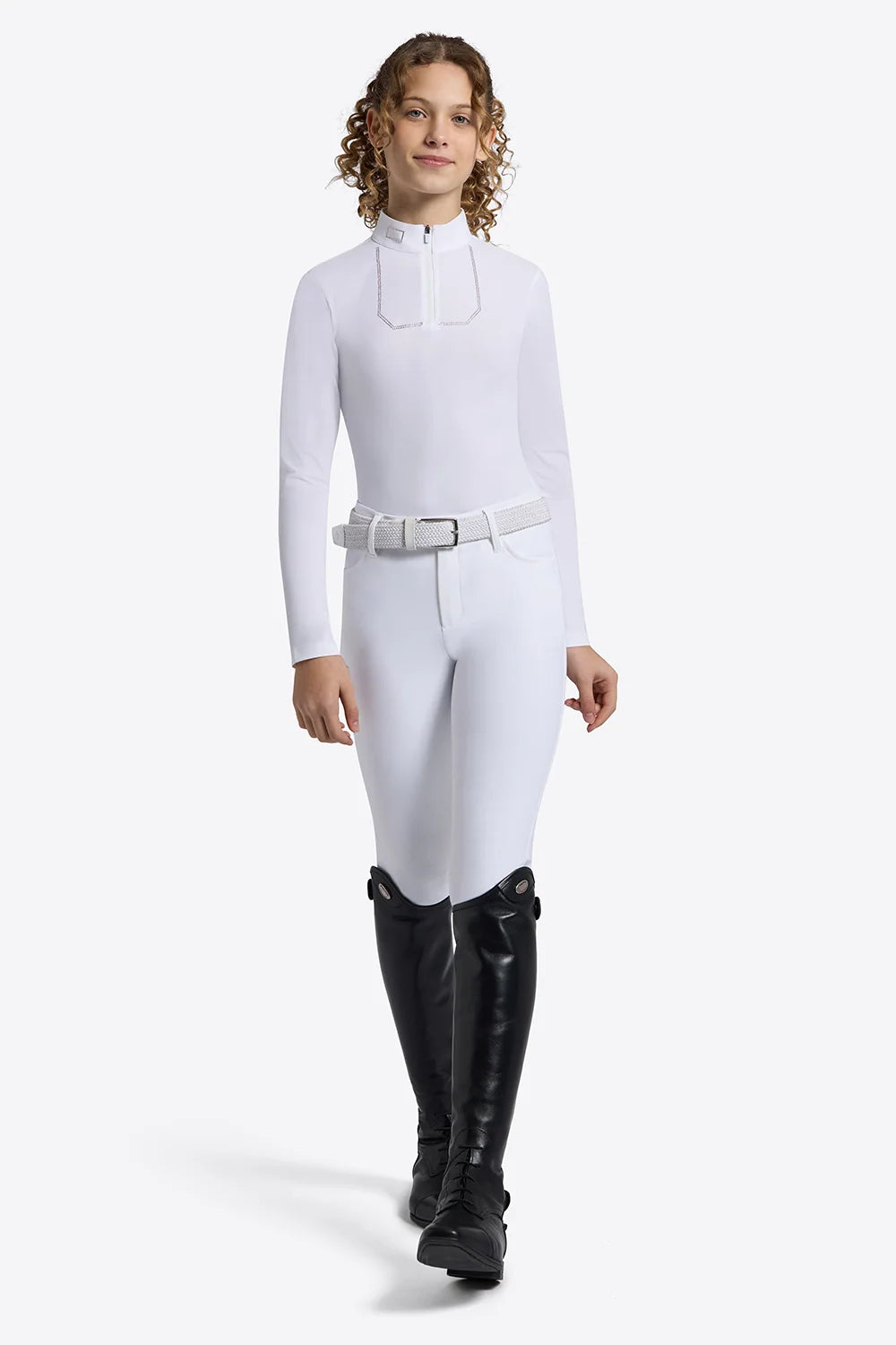 A model wearing a white long-sleeve equestrian-style riding crop top with a collar and a matching white belt, paired with black riding boots, against a light gray studio background.